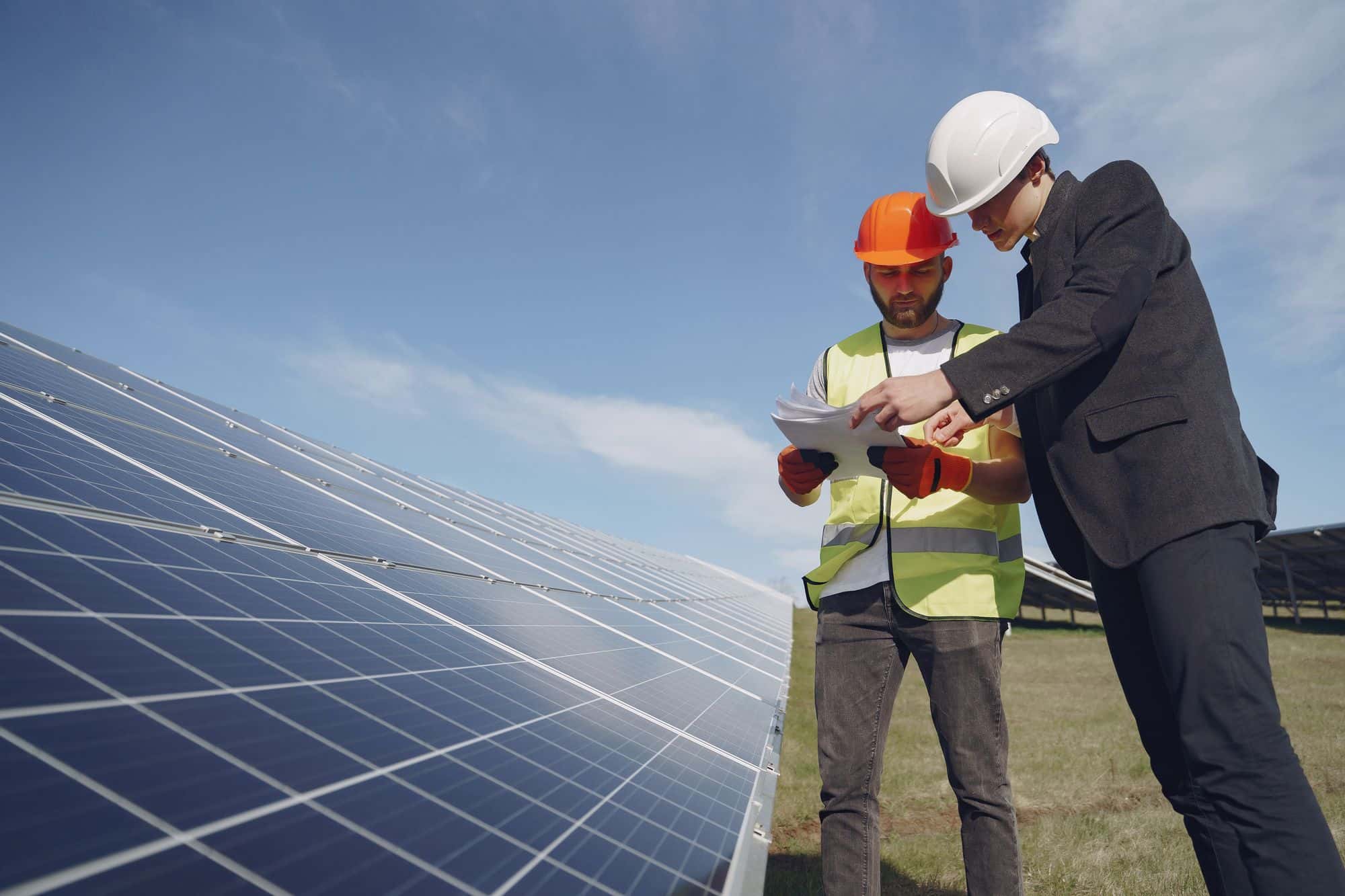 Ingénieur et technicien examinant les documents d'une étude devant des panneaux photovoltaïques